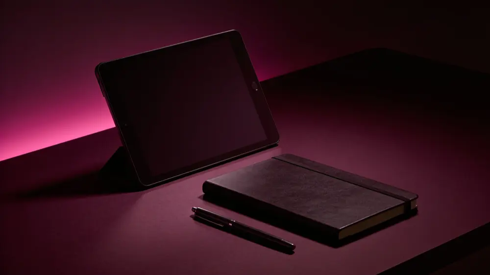 A dimly lit desk with a tablet, notebook, and pen used for this review